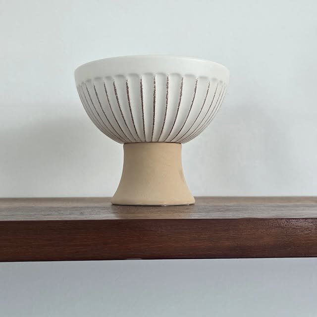 Ribbed ceramic bowl displayed on a wooden shelf